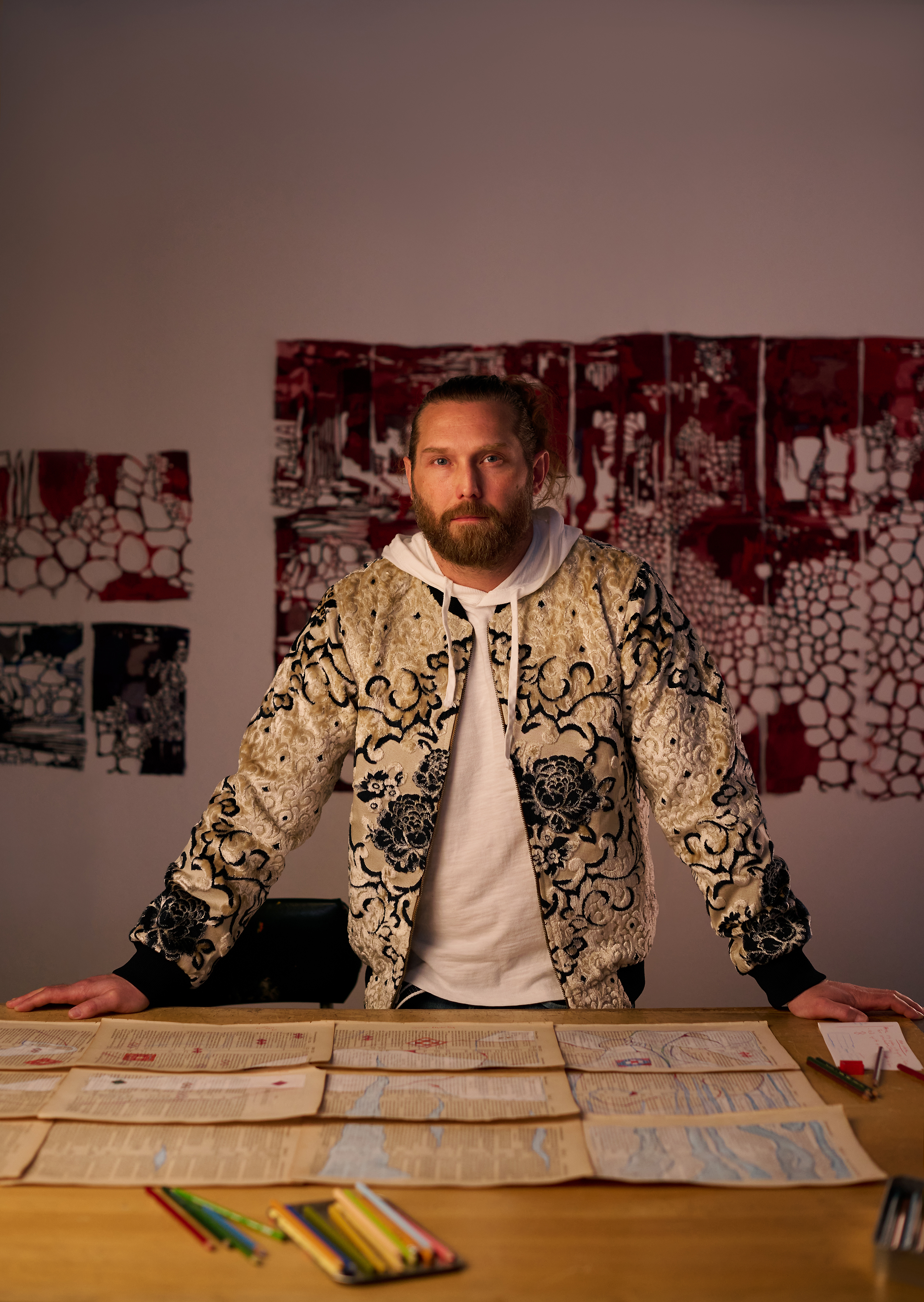 Man wearing a patterned jacket stands at a table with drawings laying out on the surface in front of him.
