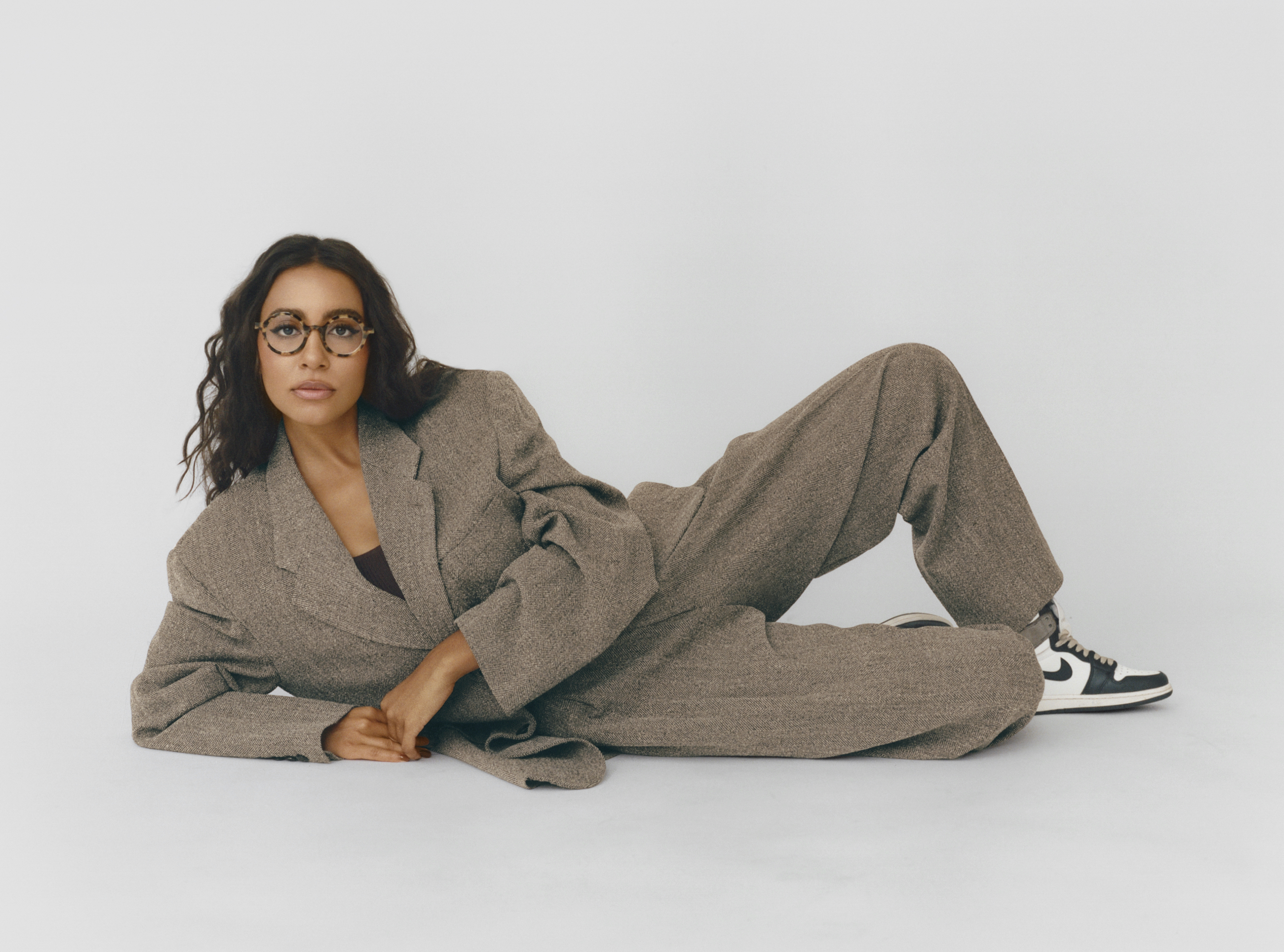 Portrait of Hannah Traore wearing a tan two-piece suit set and sneakers, laying on a seamless white backdrop.