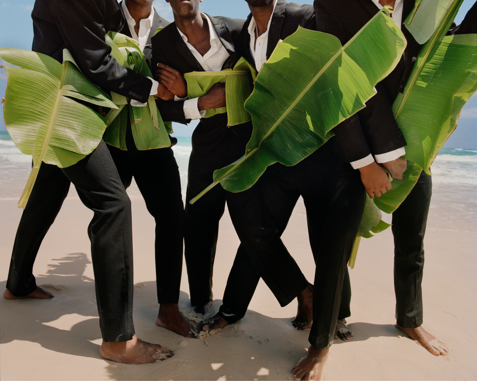 Five men dressed in suits holding palm branches on a beach. 