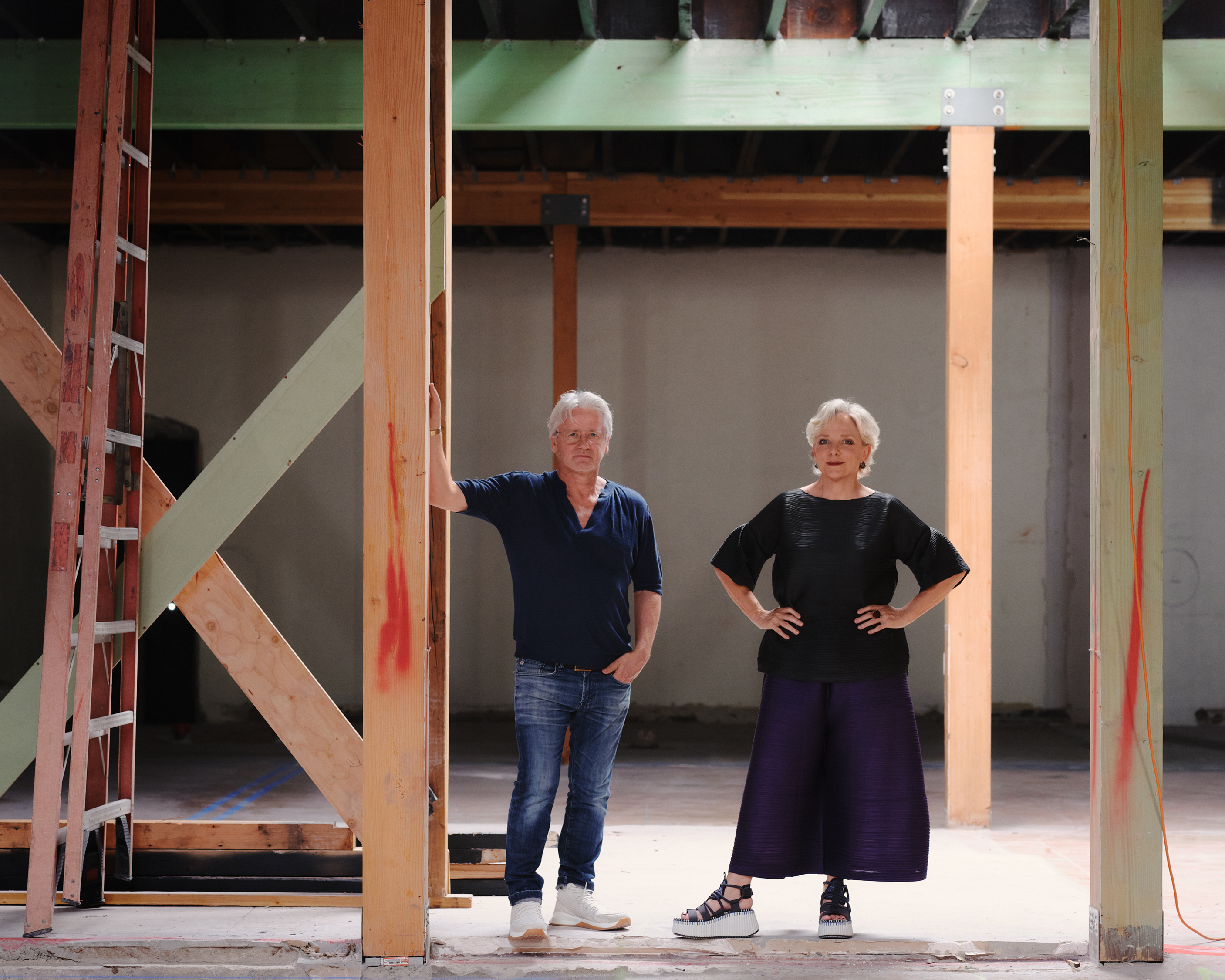 Two people (Trevyn and Julian McGowan) stand in the center of a large room with tall ceilings and large vertical beams.