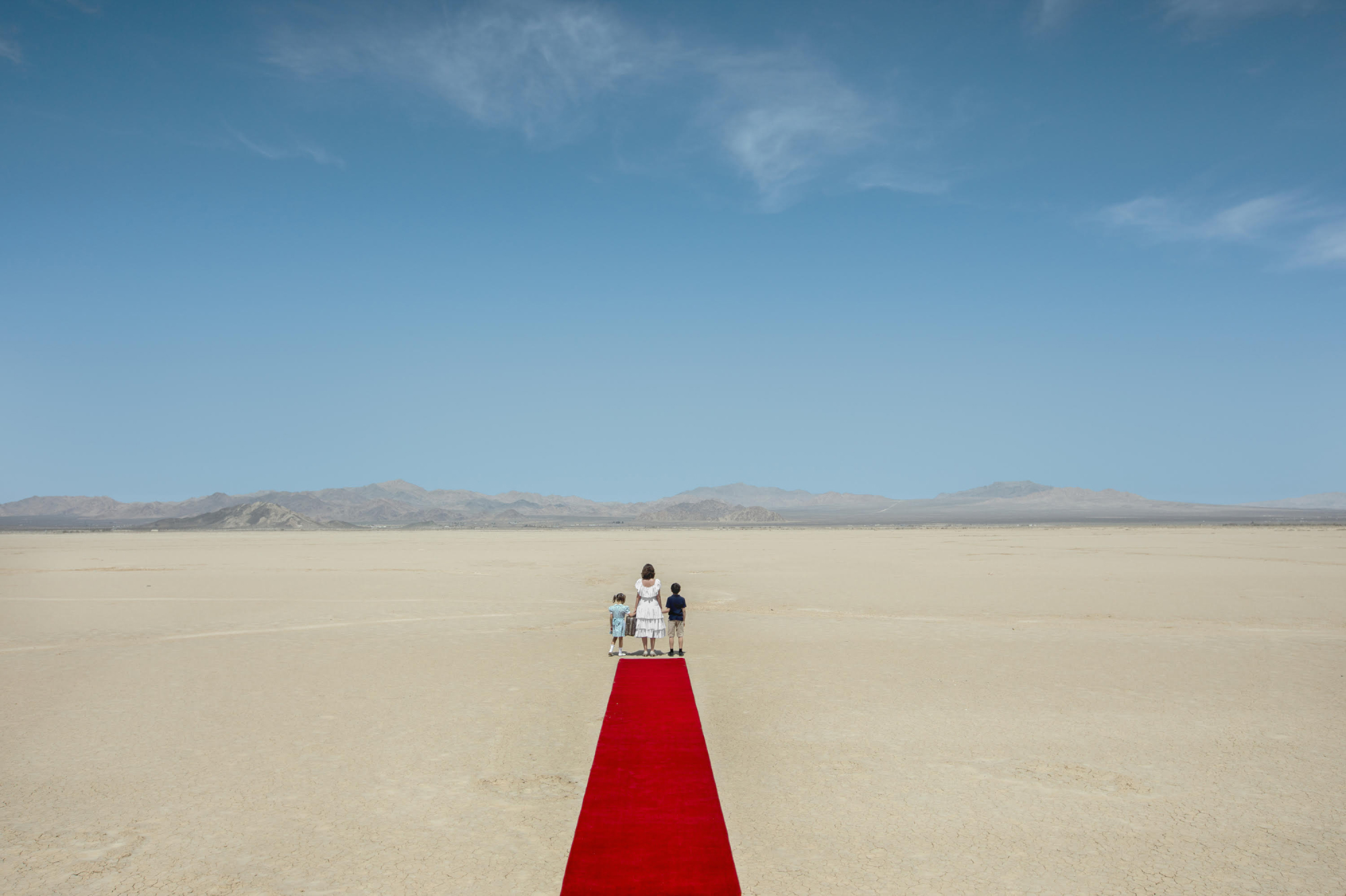 Expansive desert vista with a single red carpet stretching into the distance, and three figures standing at the edge of the carpet.