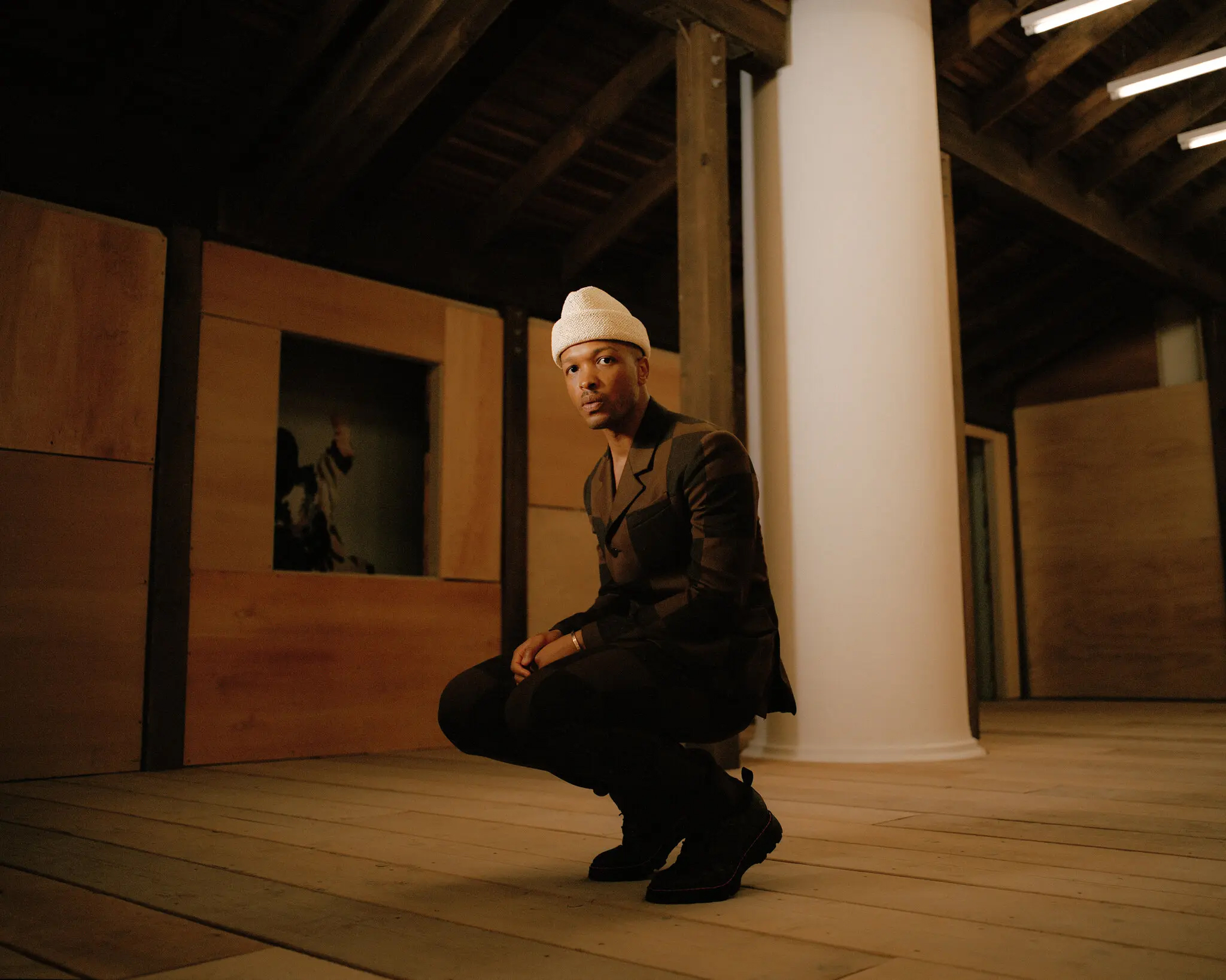 Portrait of Antwaun Sargent crouching in a gallery space, looking directly at the camera.