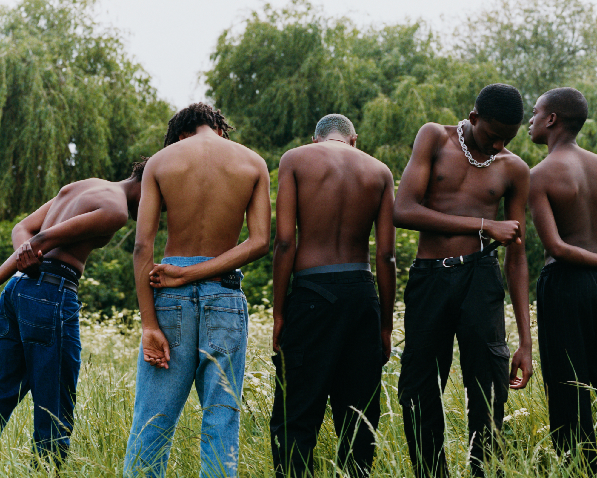 Photograph by Tyler Mitchel of five shirtless men standing in a field with their back towards the camera.